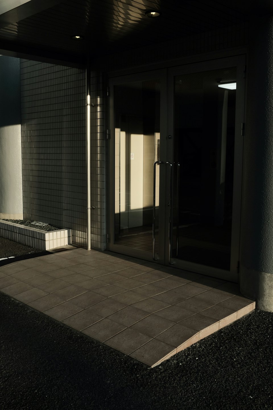 Glass entrance doors with a ramp leading from gravel.