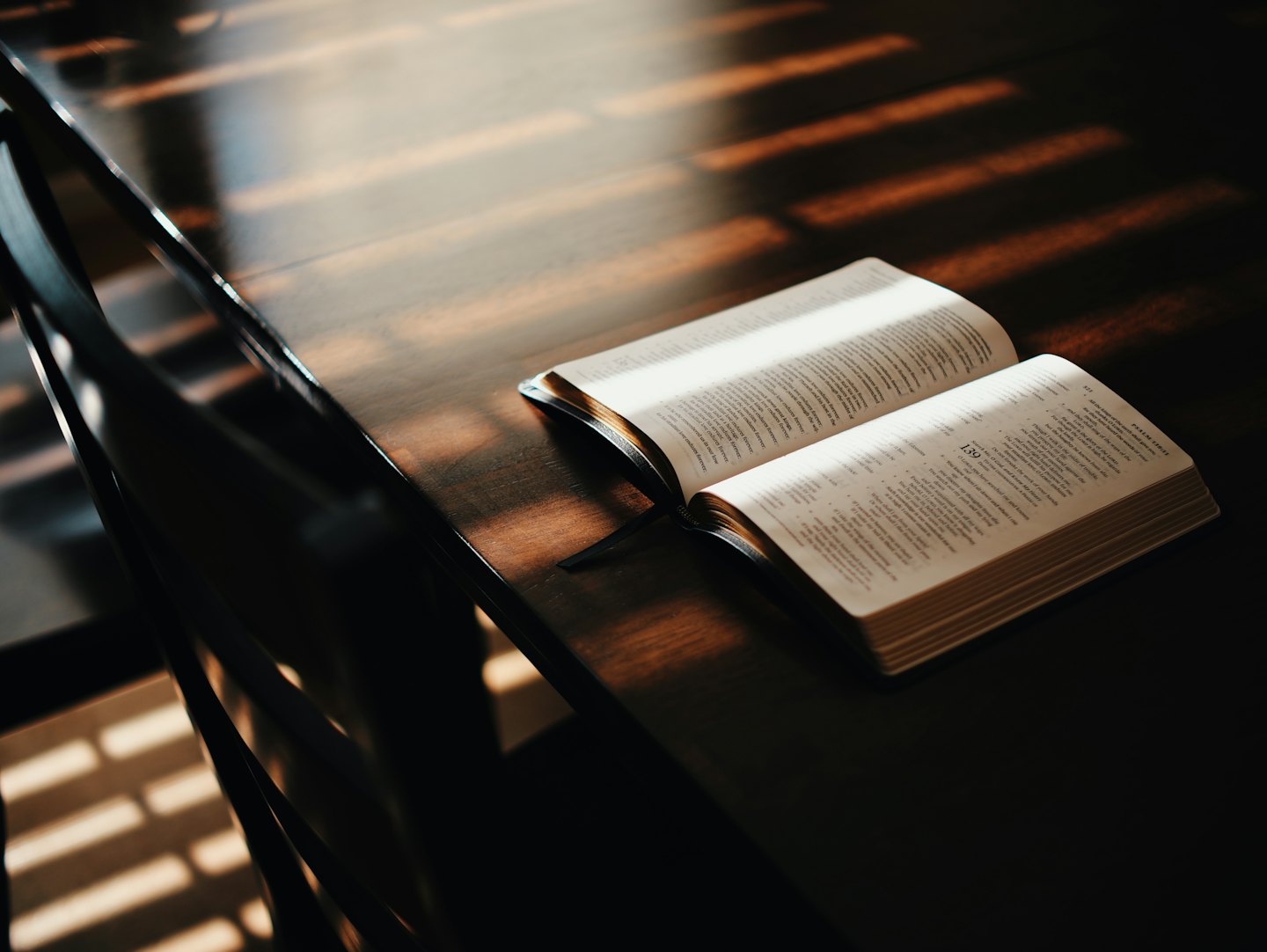 An open bible rests on a dark wooden table with sunlight on pages.