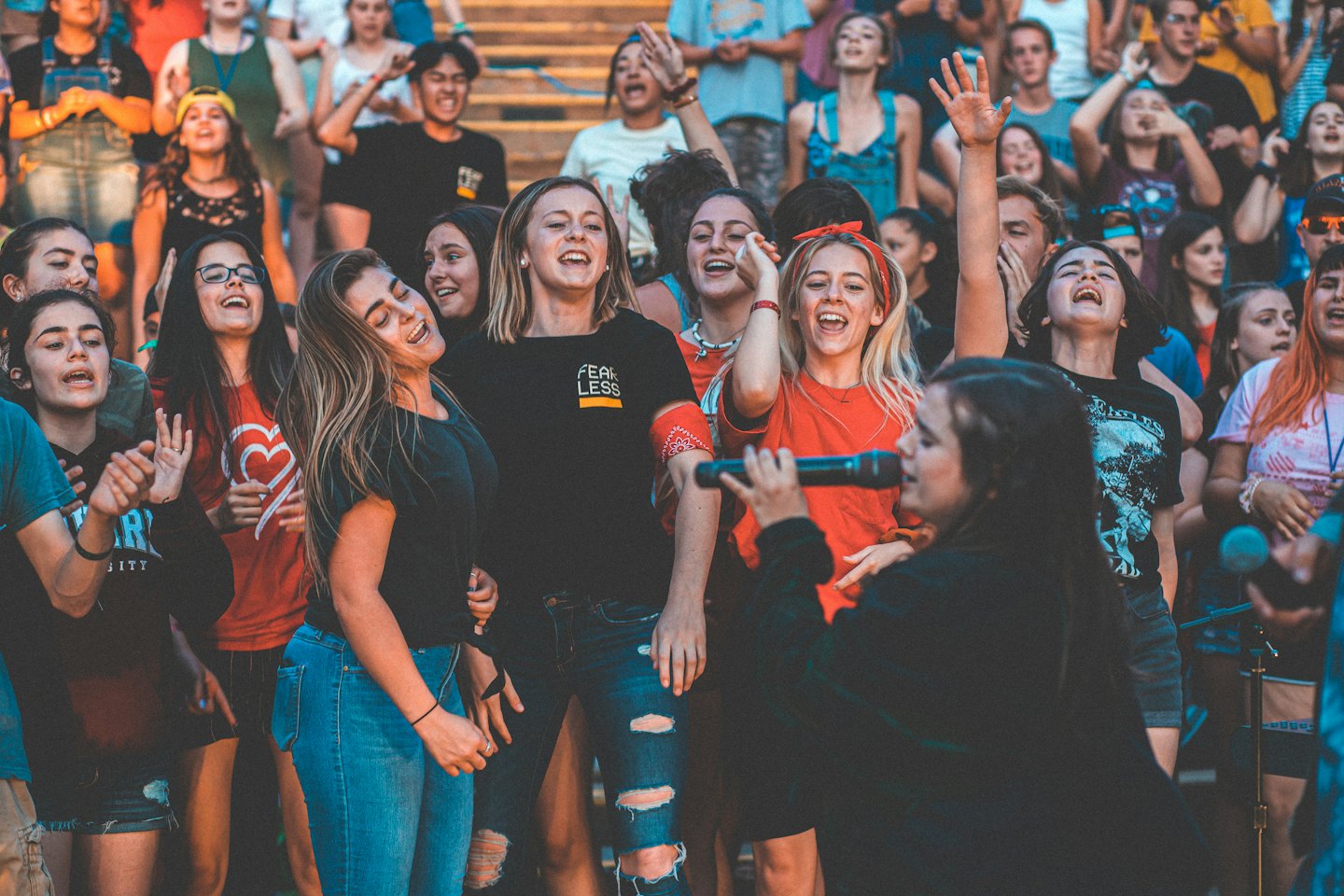 Young adults singing along with a woman holding a microphone at an outdoor event.