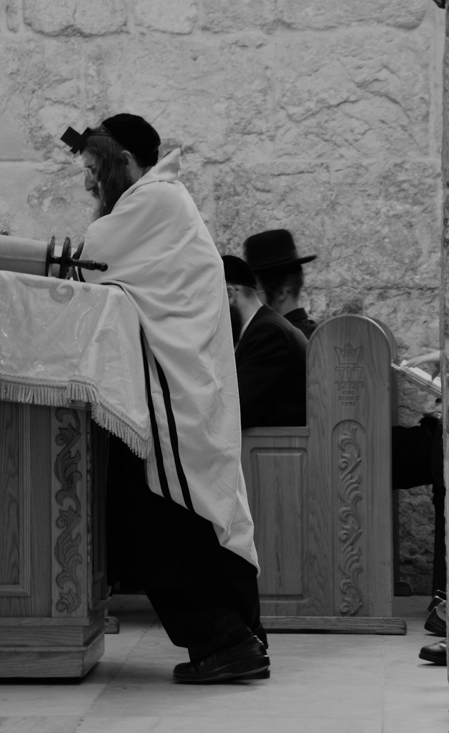 Man wearing a prayer shawl reads from a Torah scroll.