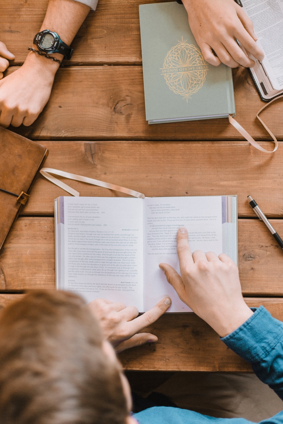 People discussing a book around a rustic wooden table.